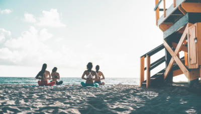 Women practicing yoga on a beach next to a lifeguard tower